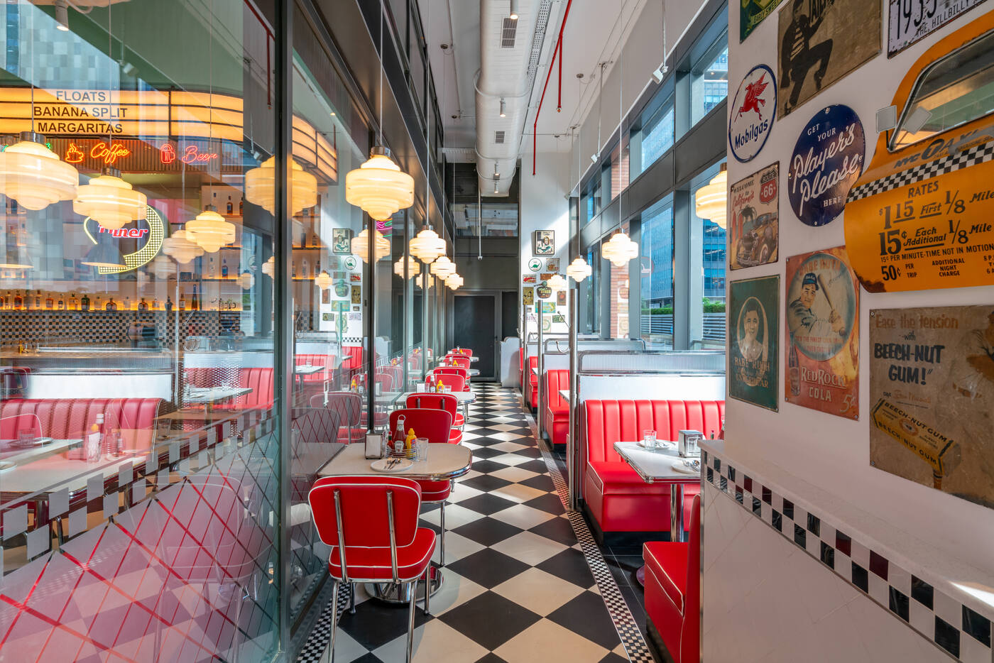 Row of red vinyl booths on a checkerboard floor with vintage American tin signs at the All American Diner Hyderabad