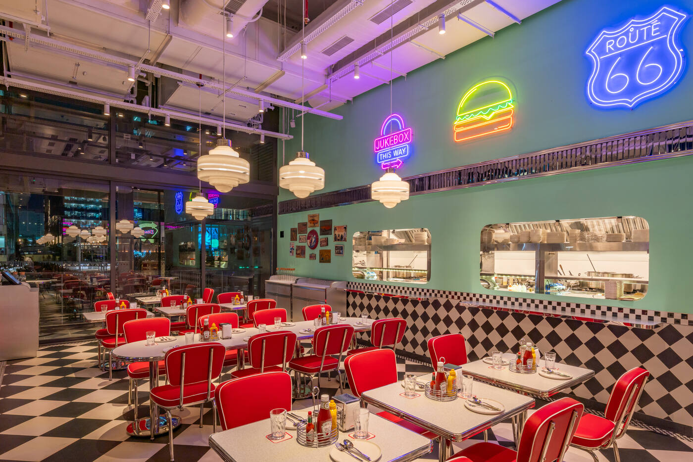 Route 66 and burger neon signs above red chairs and an open kitchen window at the All American Diner Hyderabad
