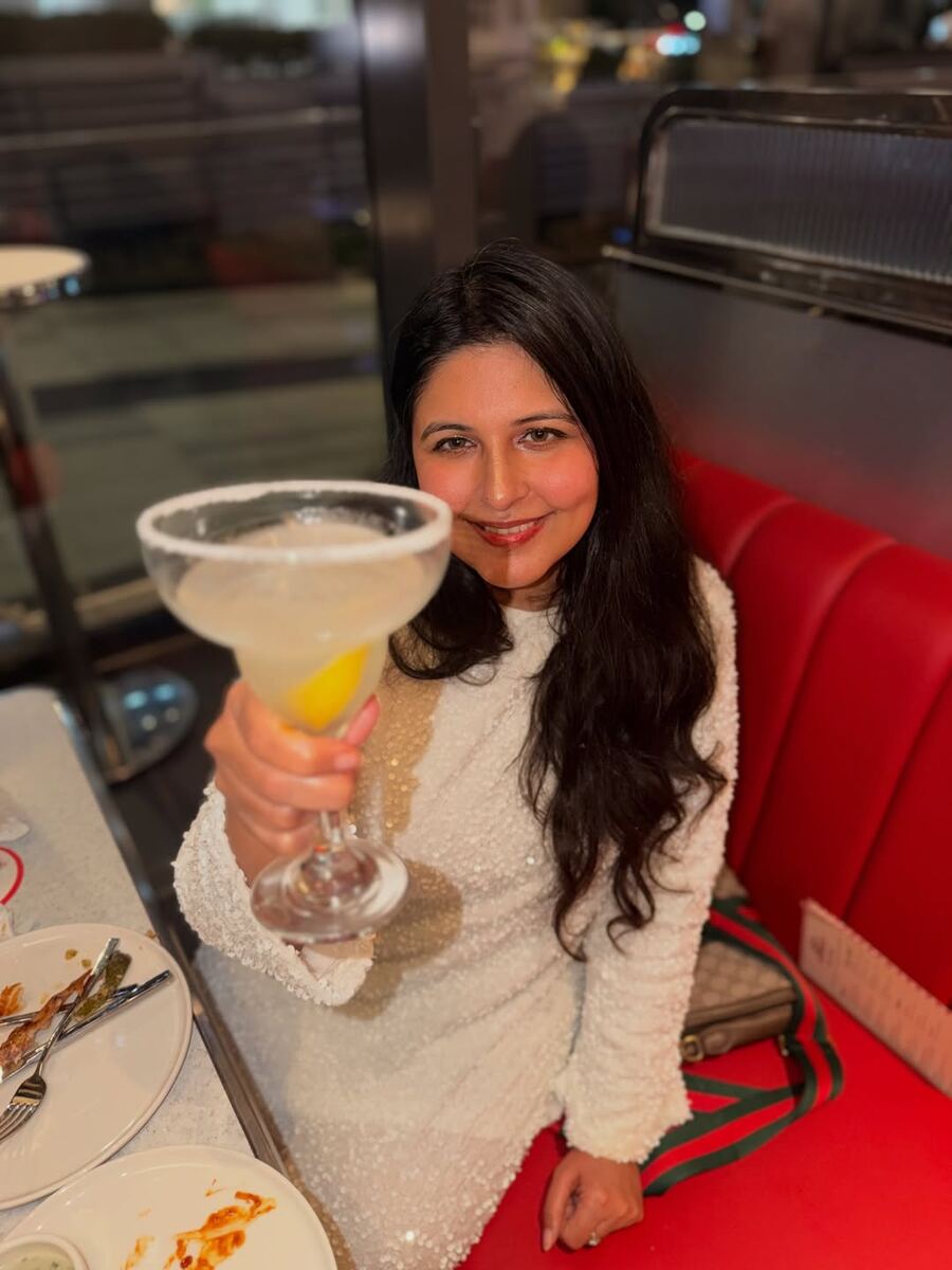 Reema holding a salt-rimmed margarita in a red booth at the All American Diner Hyderabad
