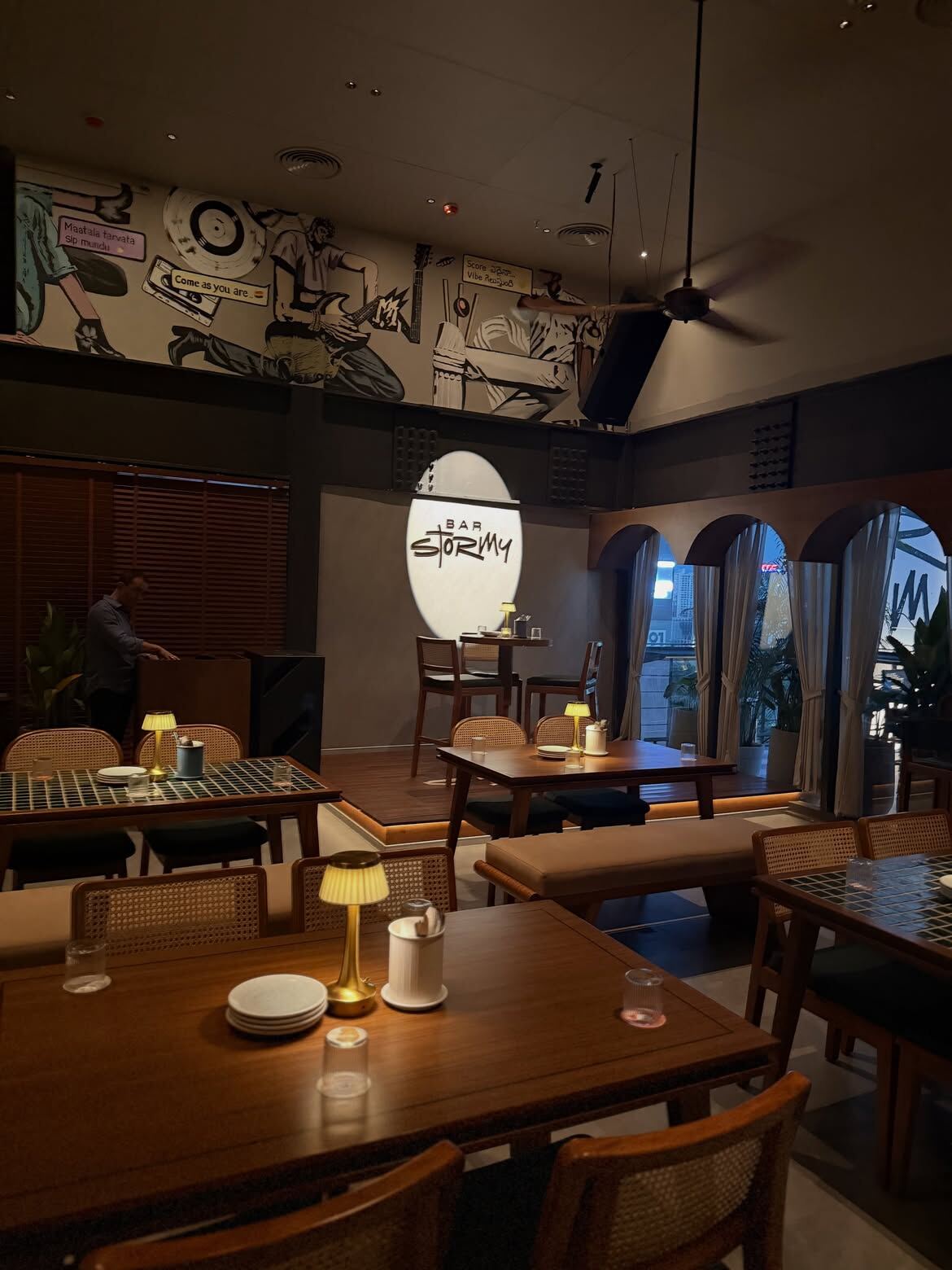 Bar Stormy interior, Financial District, Hyderabad — warm wood tables, vintage lamps, and comic-style wall mural