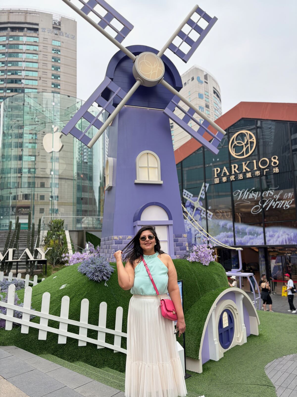 Reema in front of a giant purple windmill installation outside the PARK 108 mall in Jiefangbei, Chongqing, with the Apple store glass cube behind