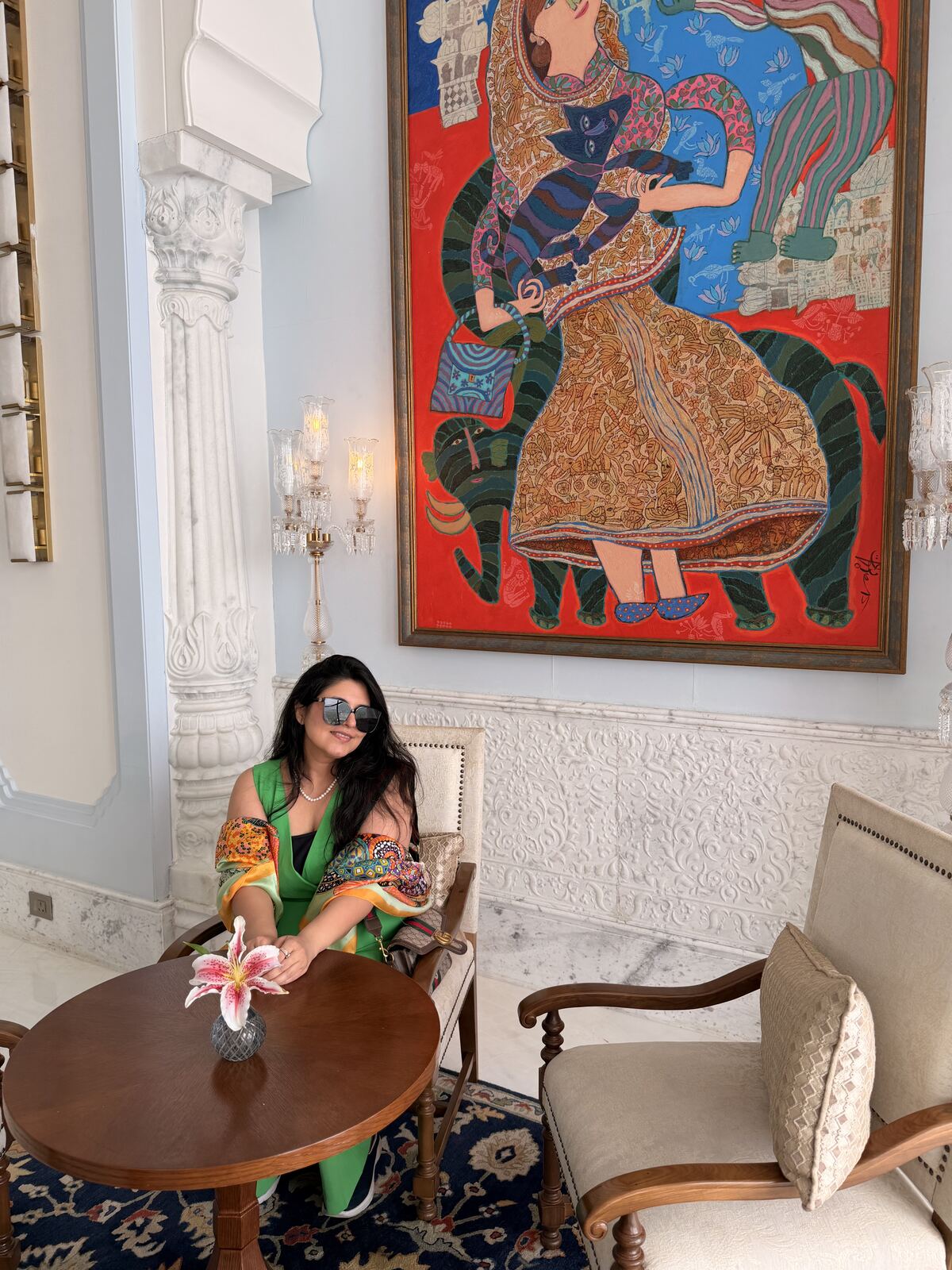 Reema seated in the lounge area of Fairmont Udaipur Palace next to a colourful painting