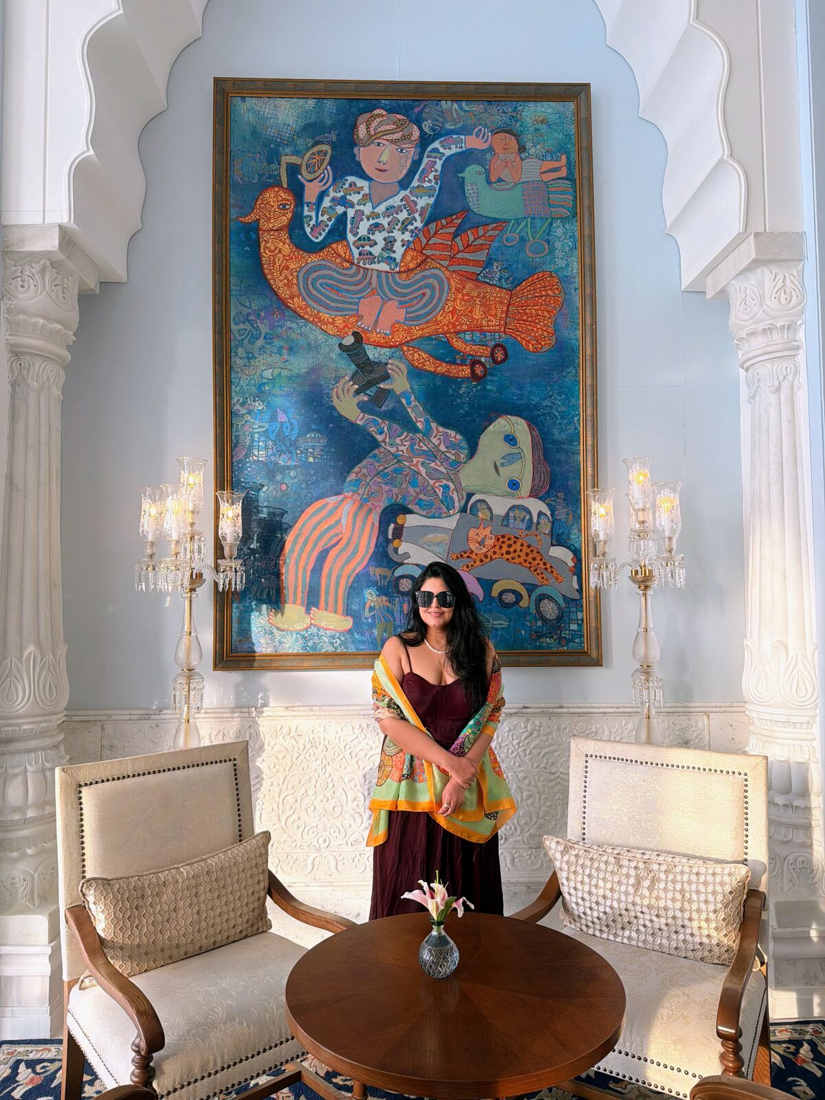 Reema seated beneath a large Rajasthani-style painting in the Fairmont Udaipur Palace lobby