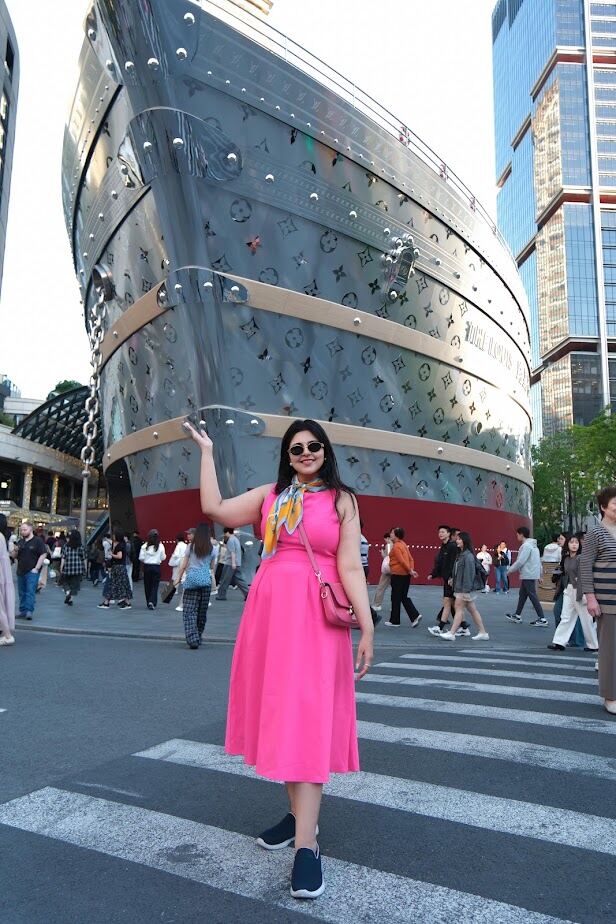 Reema in a pink dress standing in front of the Louis Vuitton ship-shaped store in Shanghai