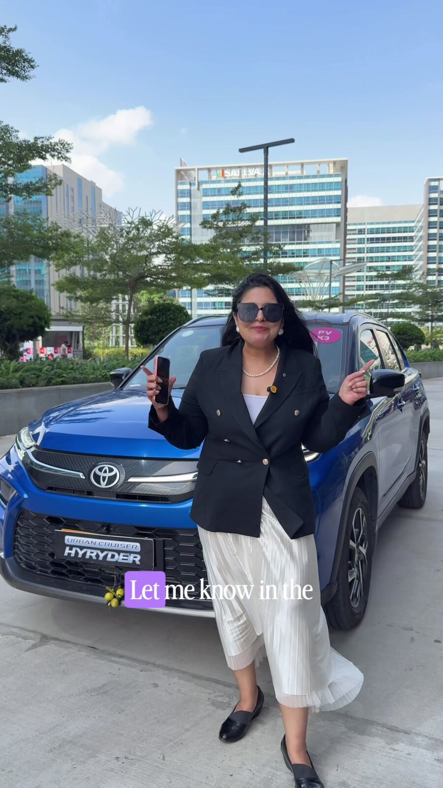 Reema posing with the Toyota Urban Cruiser Hyryder hybrid SUV in front of the Hyderabad skyline, asking whether readers would pick a hybrid over a diesel